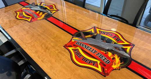 This fire station furniture piece features a conference table adorned with custom graphics, showcasing the Dannelly Field Fire Dept. emblem on a rich wood surface.