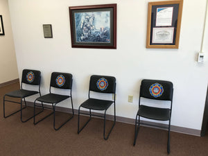 Four black custom firehouse chairs with the fire department logo on the front of the chair lined up on a wall in a fire station