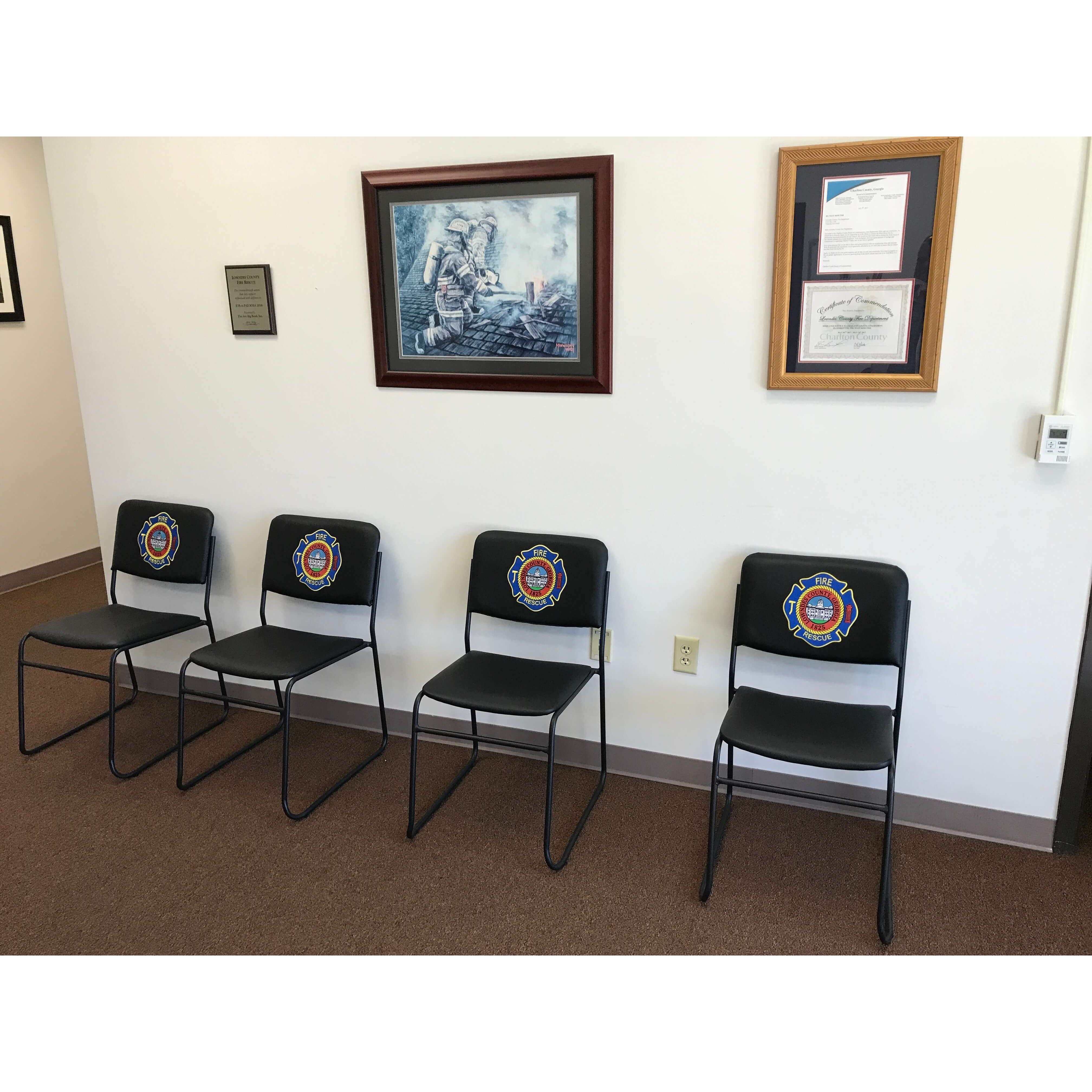 Four black custom firehouse chairs with the fire department logo on the front of the chair lined up on a wall in a fire station